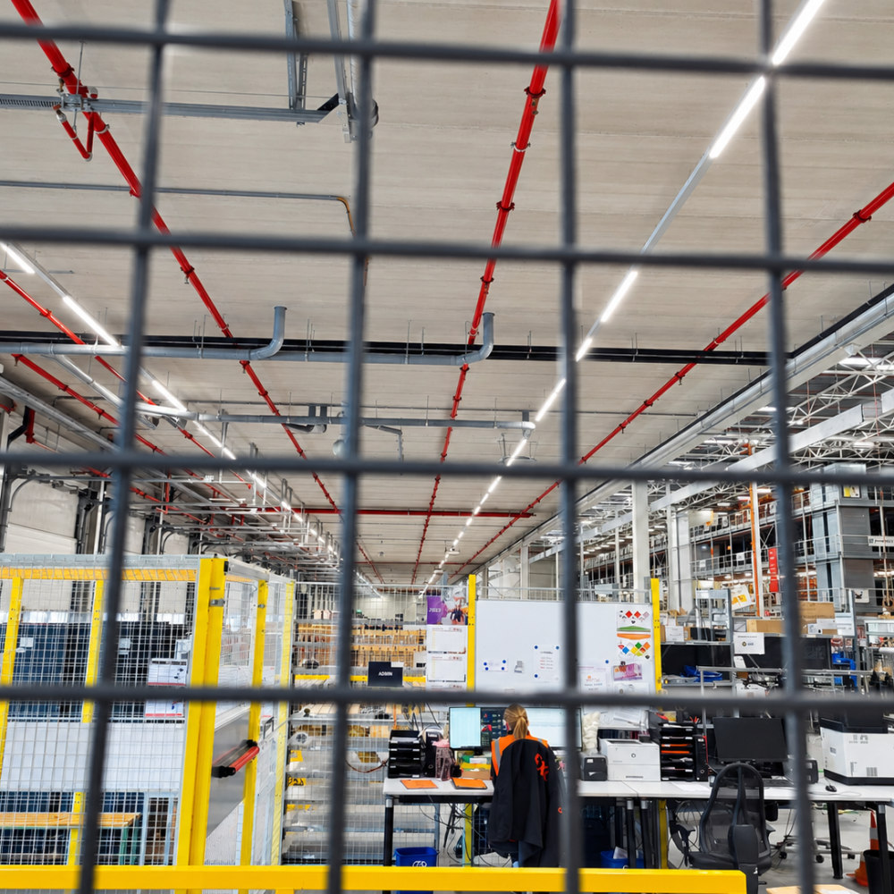 Magazijnhal met kantoorwerkplekken achter een hekwerk