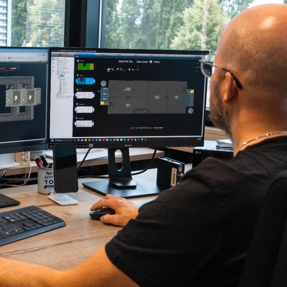 Medewerker bewaakt een gebouwbeheersysteem op twee beeldschermen