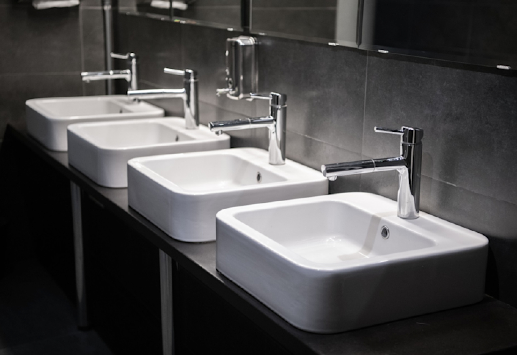 Rij witte wastafels met kranen in een sanitaire ruimte